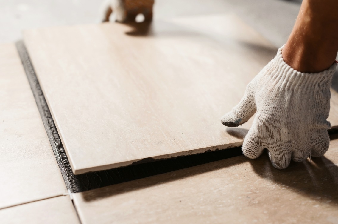 The hands of the tiler are laying the ceramic tile on the floor. Close up macro shot. Home renovation and building new house concept