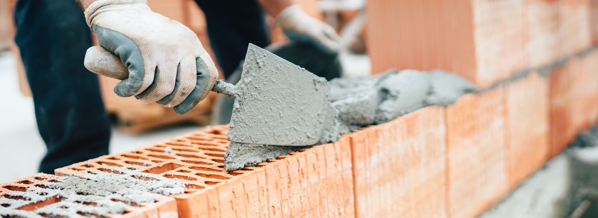 Professional worker using pan knife for building brick walls with cement and mortar